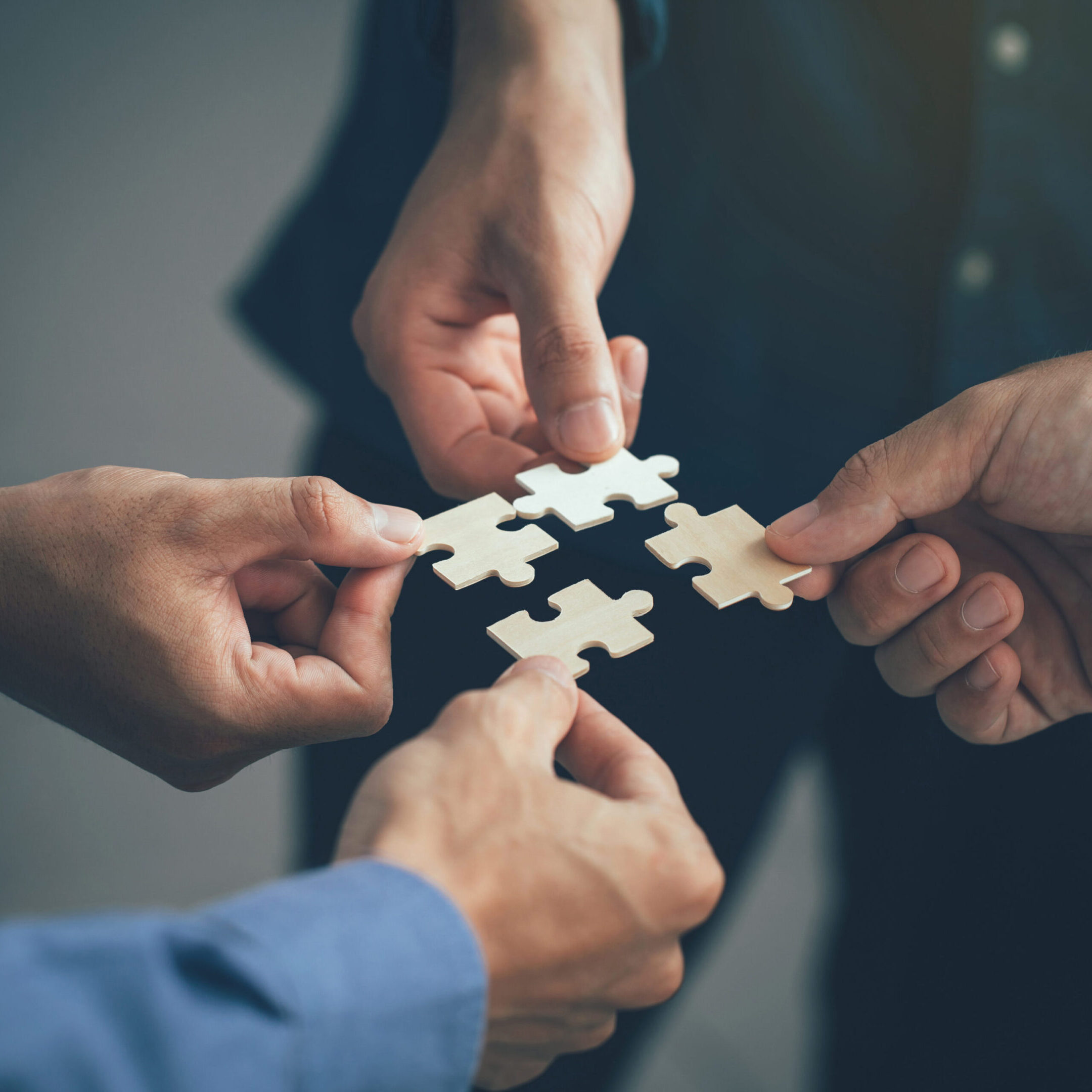 Four hands collaboratively connecting puzzle pieces.